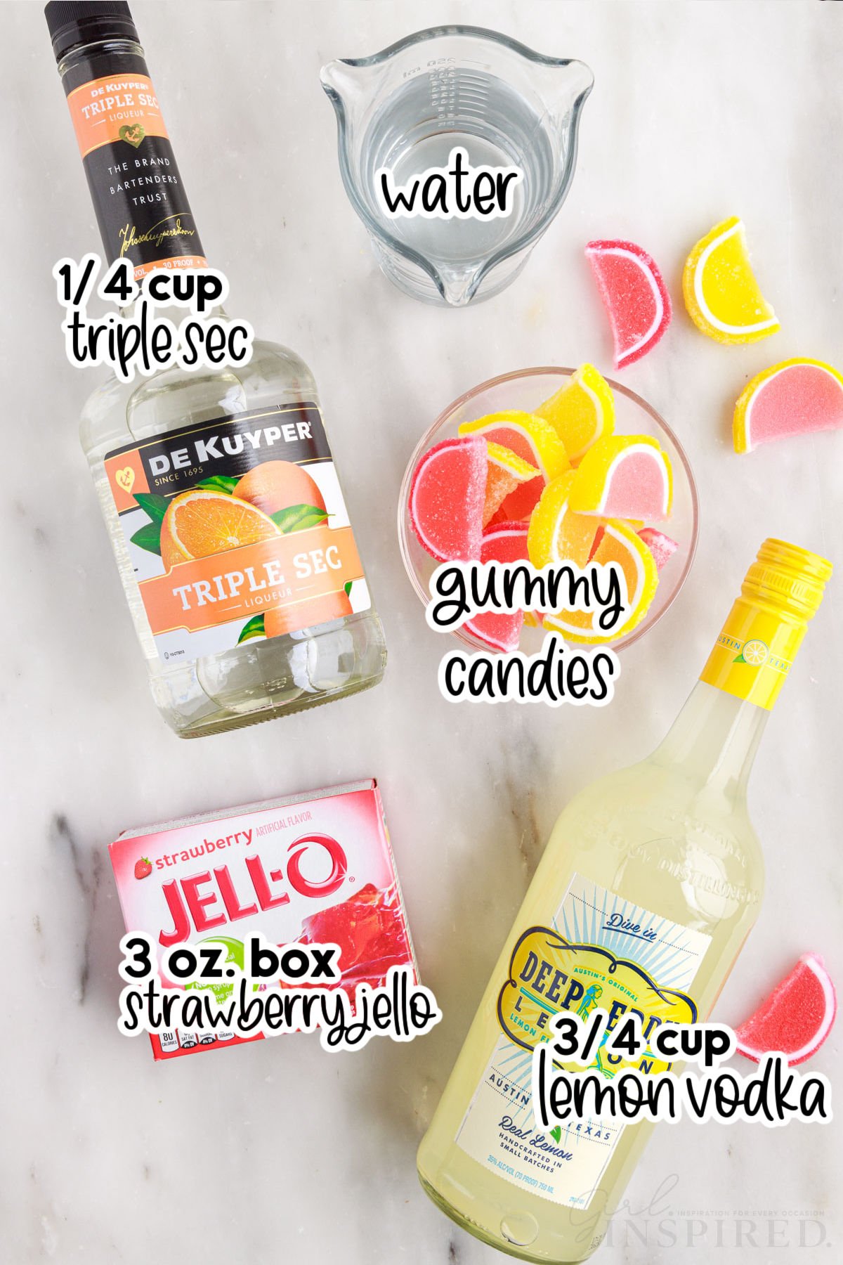 Individual ingredients for pink lemonade jello shots: strawberry jello, triple sec, cup of water, bowl of gummy candies, and lemon vodka with text labels.
