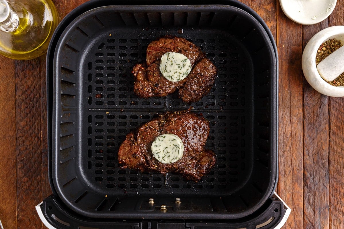 two cooked filets in an air fryer basket, both topped with butter compound