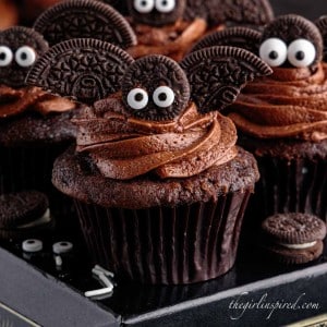 close up of a bat cupcake on a black box with other bat cupcakes surrounded by edible eyes and mini oreos