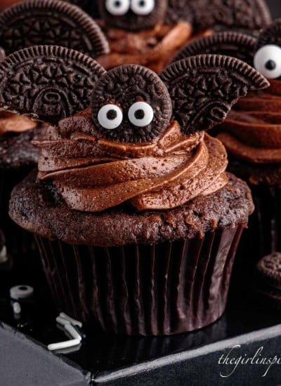 close up of a bat cupcake on a black box with other bat cupcakes surrounded by edible eyes and mini oreos