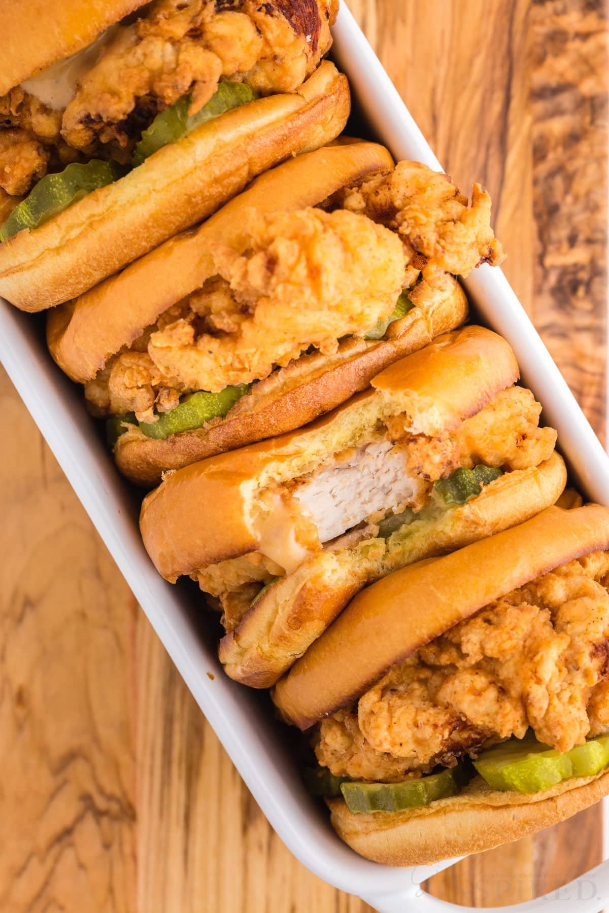 Fried chicken sandwiches stacked on their sides in a white loaf pan.