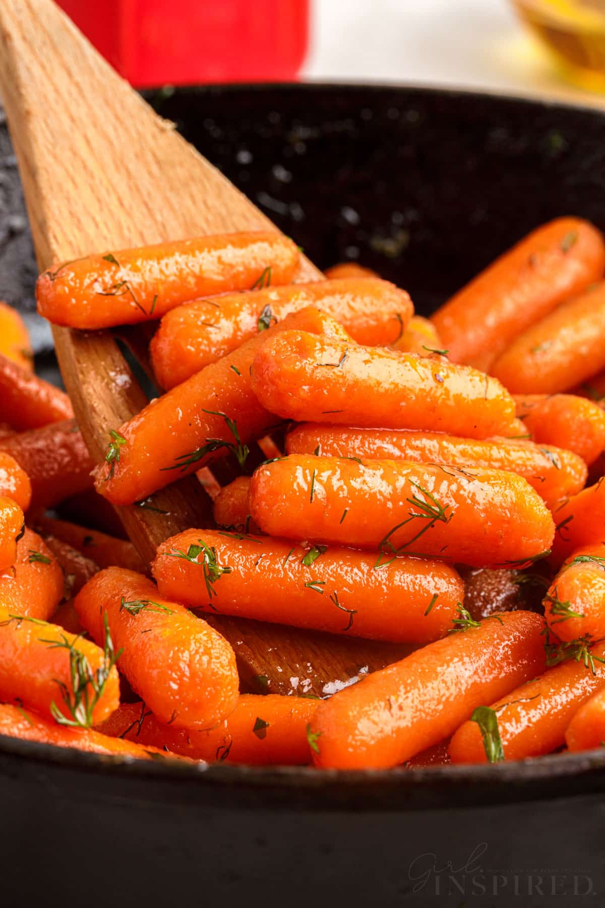 side view of a wooden spatula scooping some brown sugar honey glazed carrots