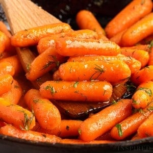 brown sugar honey glazed carrots in a skillet on a wooden spoon