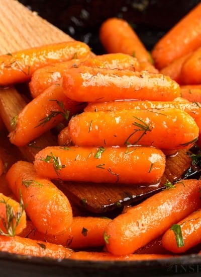 brown sugar honey glazed carrots in a skillet on a wooden spoon