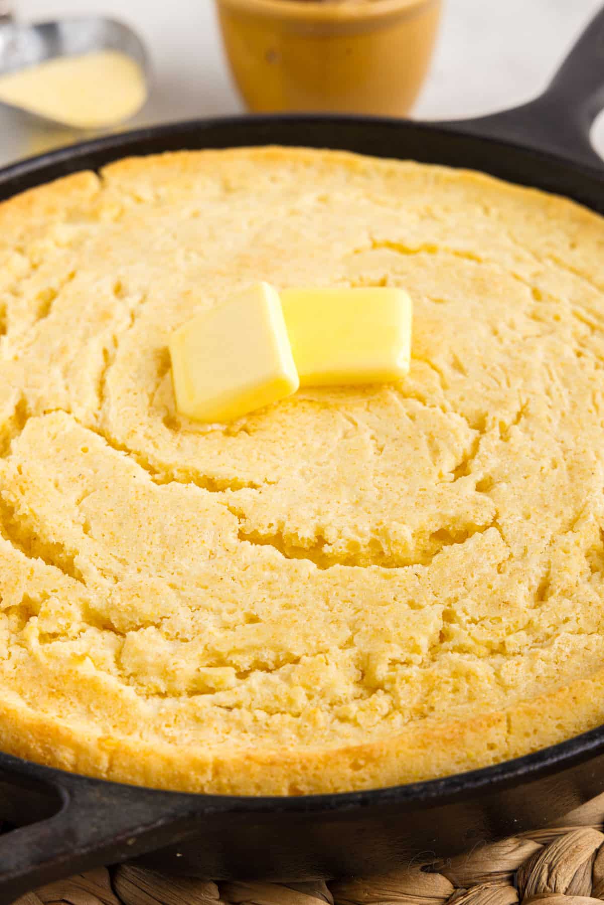 side view of cornbread in a skilled with 2 slices of butter on top