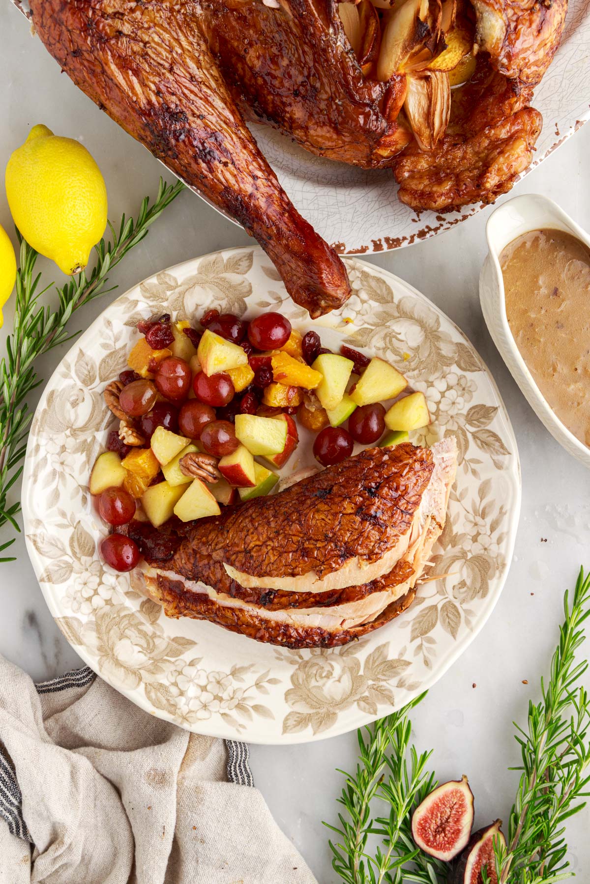 slices of the browned smoked turkey on a plate with a large side of mixed fruit next to gravy and bottom of turkey