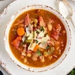 top view close up of 15 bean soup sprinkled with shreds of cheese in a bowl next to a spoon