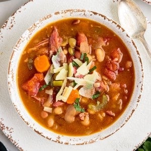 top view close up of 15 bean soup sprinkled with shreds of cheese in a bowl next to a spoon