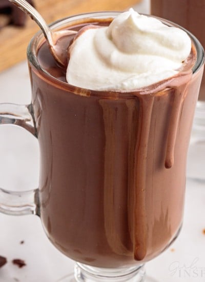 close up of a glass of italian hot chocolate topped with whipped cream with a spoon in it