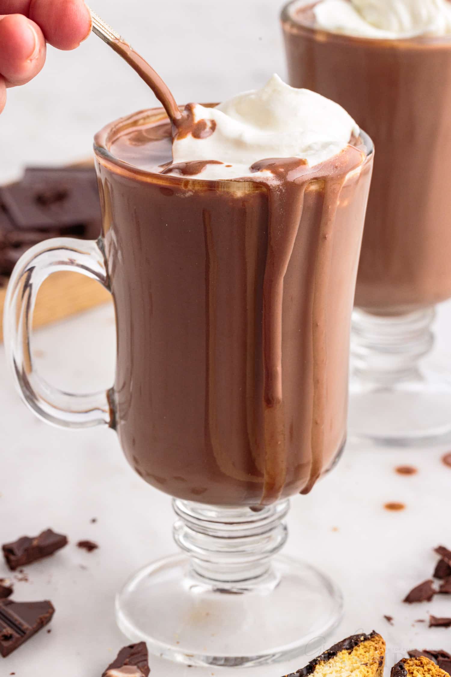 a glass of italian hot chocolate with whipped cream on top being mixed with a spoon
