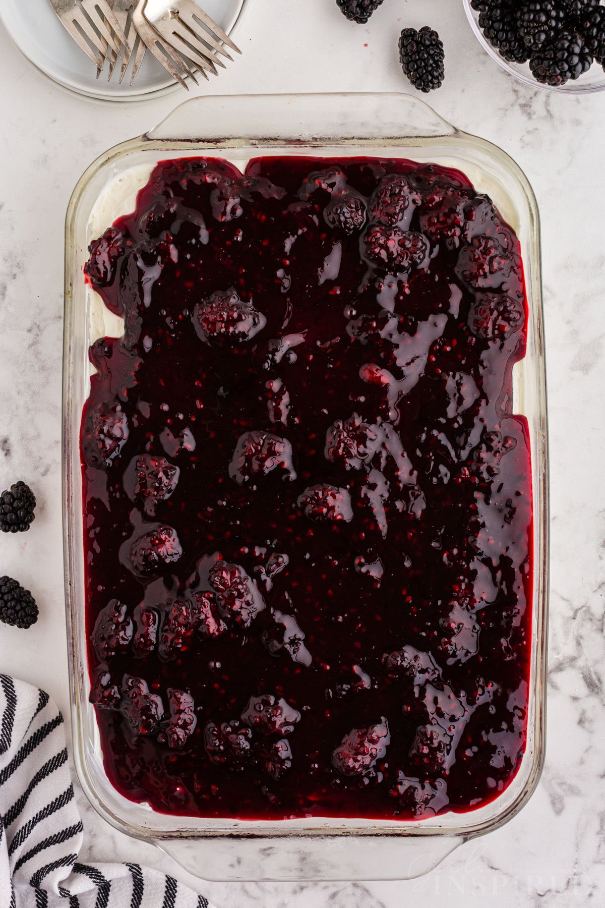 Assembled no bake blackberry cheesecake in glass baking dish, with plates, forks, and bowl of blackberries.