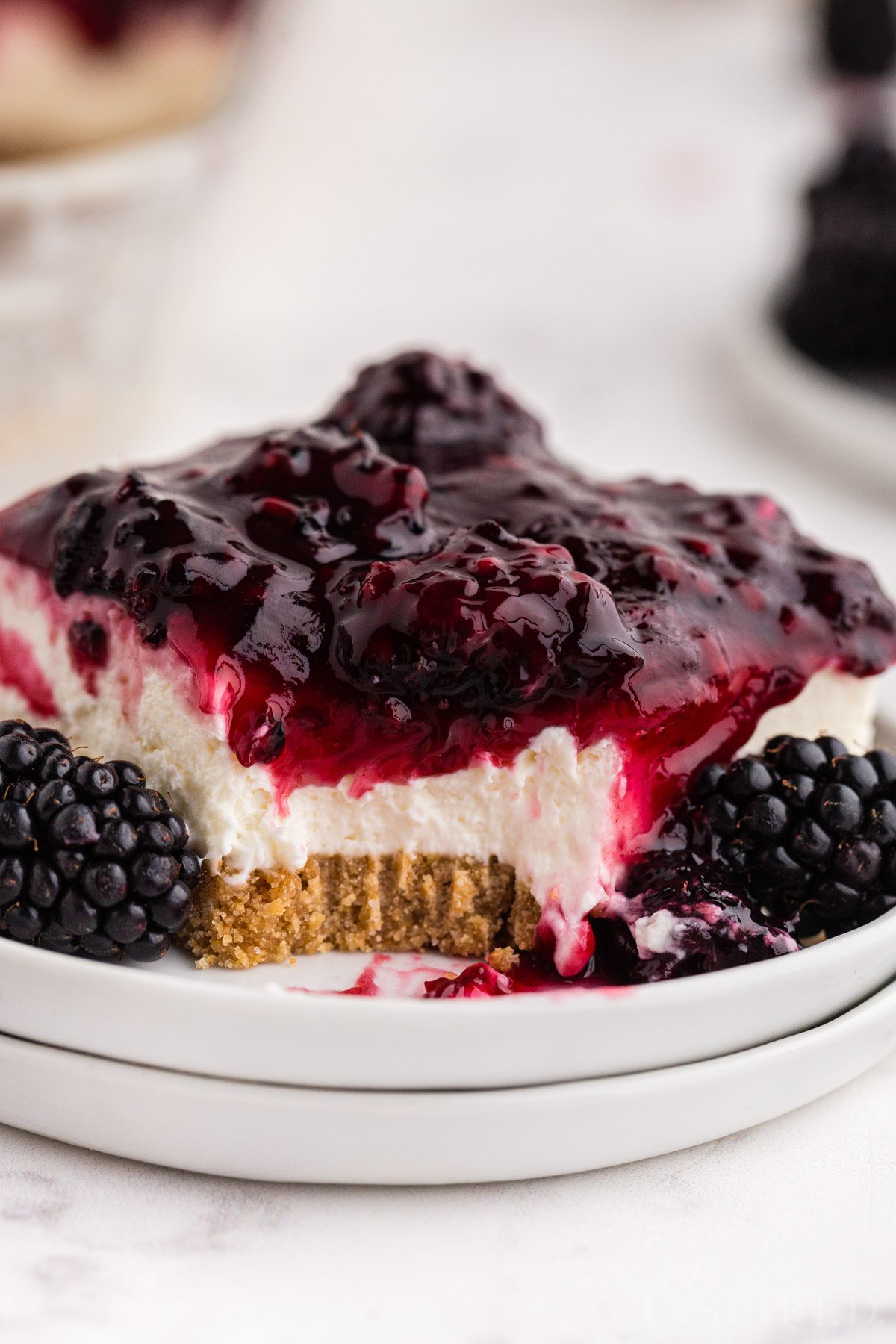Close up of a slice of no bake blackberry cheesecake with a forkful removed, on a white marble countertop.