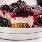 no bake blackberry cheesecake with a bite taken out showing the layers of graham cracker crust, cheesecake filling, and blackberry topping.