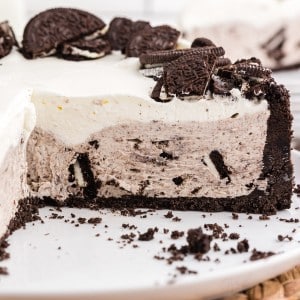 No bake Oreo cheesecake with slices removed on a white plate, on top of a woven mat, single slice of no bake Oreo cheesecake on staked white side plates in the background