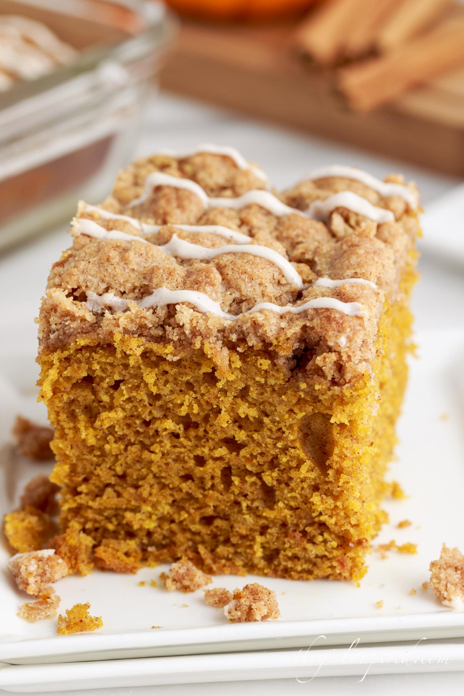 a square of pumpkin coffee cake drizzled with glaze on a plate