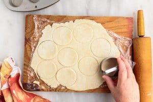 rolled out dough on cutting board with 9 circles cut from a biscuit cutter next to a rolling pin