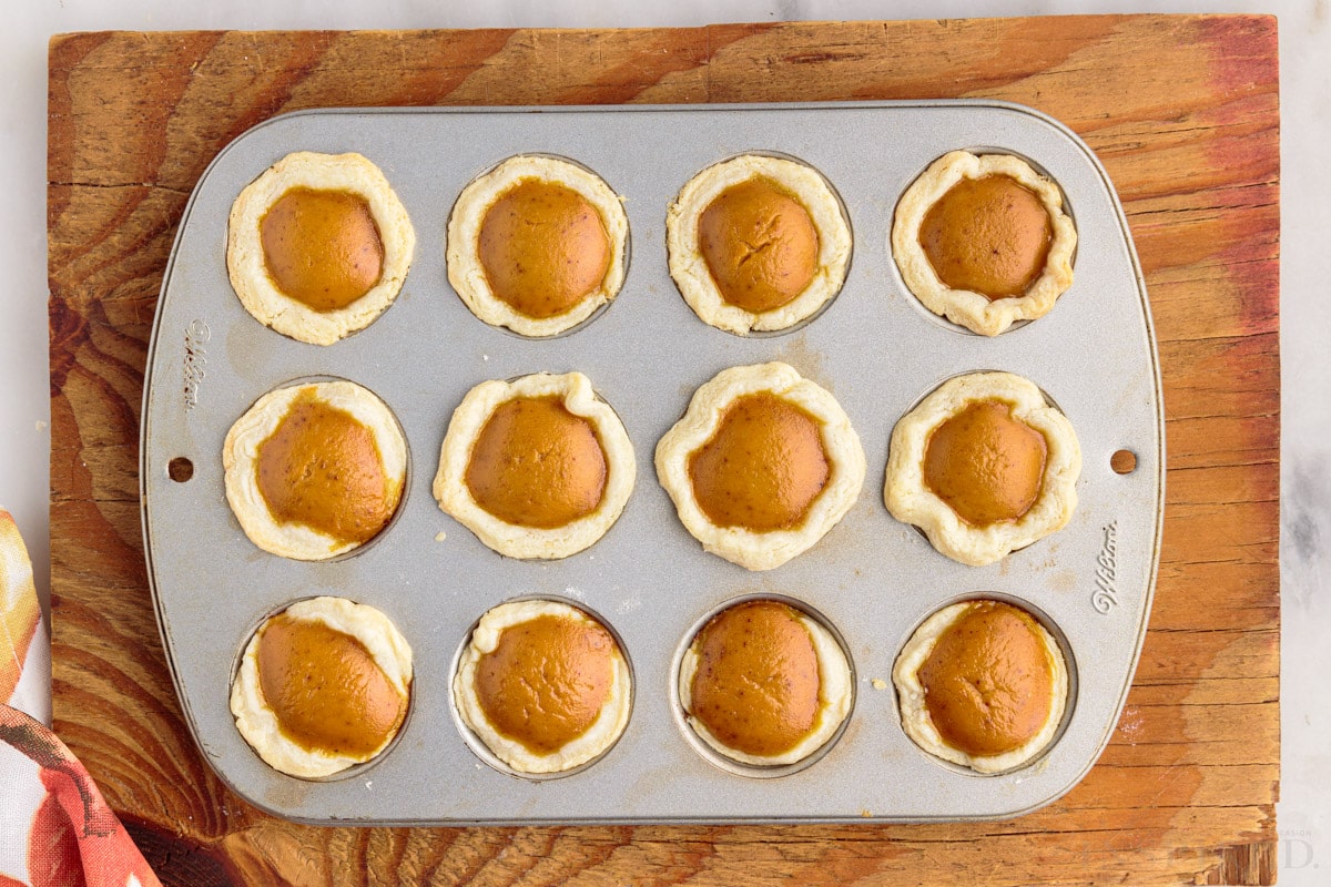 baked pumpkin pie bites in a 12 cavity muffin tin on top of a cutting board