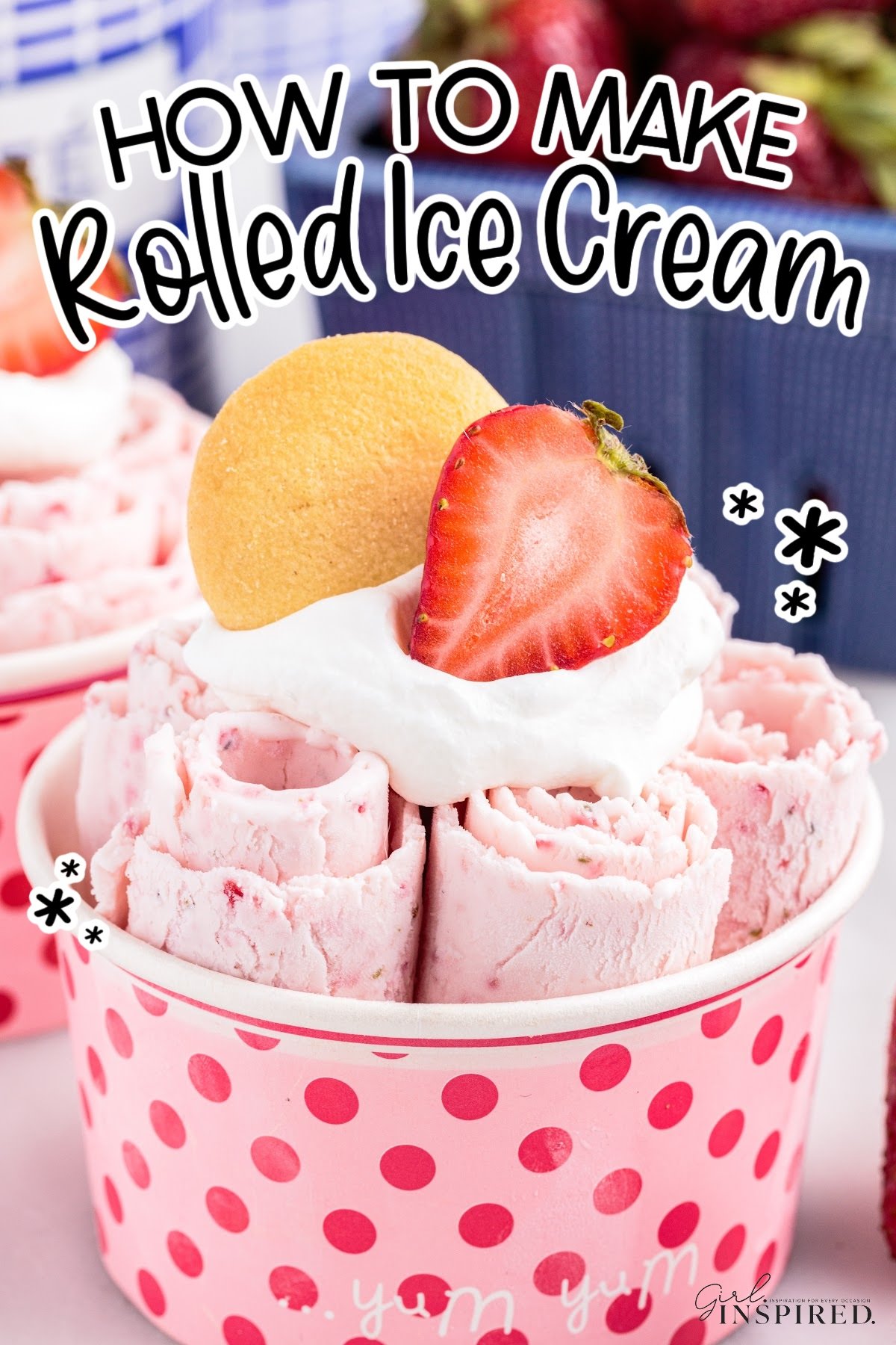 Pink polka dot cup with strawberry rolled ice cream, whipped cream, a strawberry, and a cookie on top with blue berry basket in background and text overlay "how to make rolled ice cream."