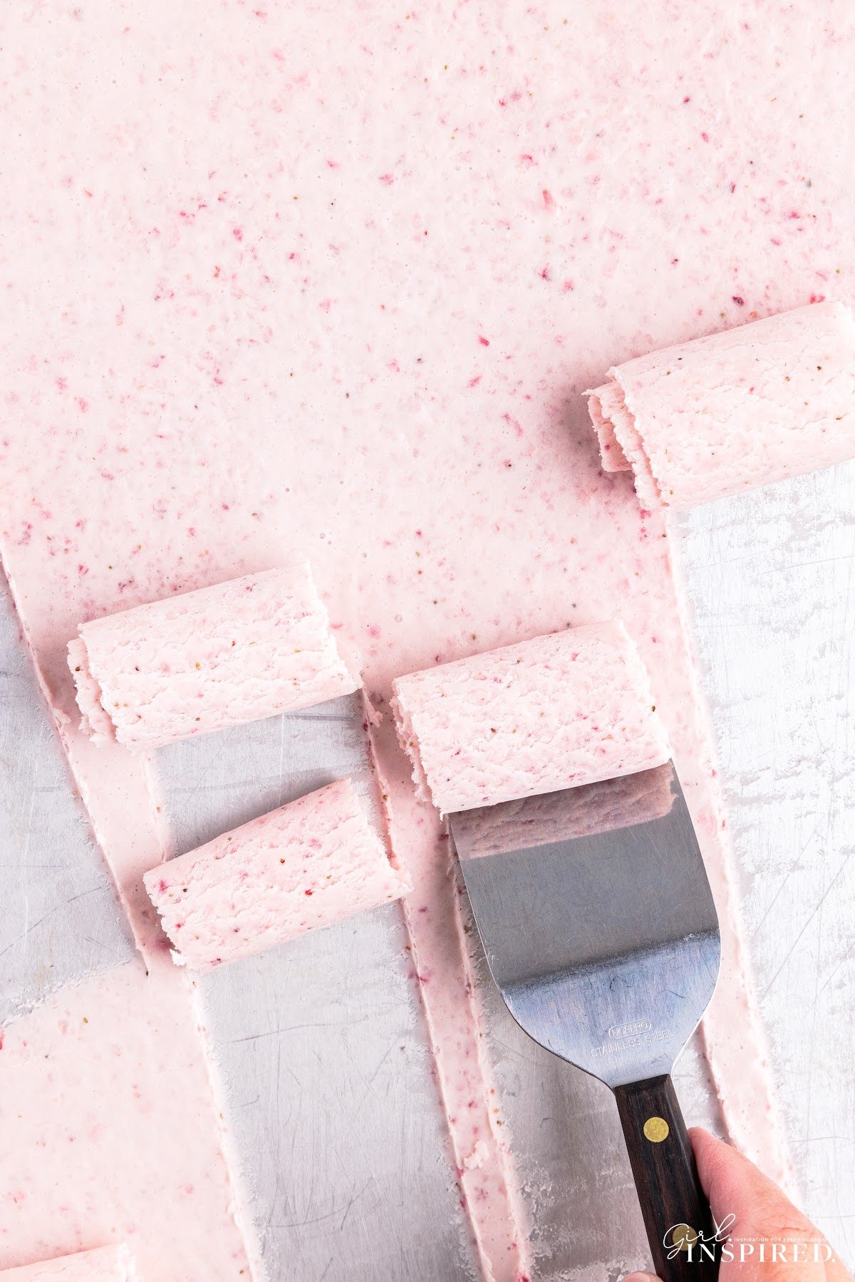 Spatula scraping rolls of strawberry rolled ice cream on a quarter sheet pan.