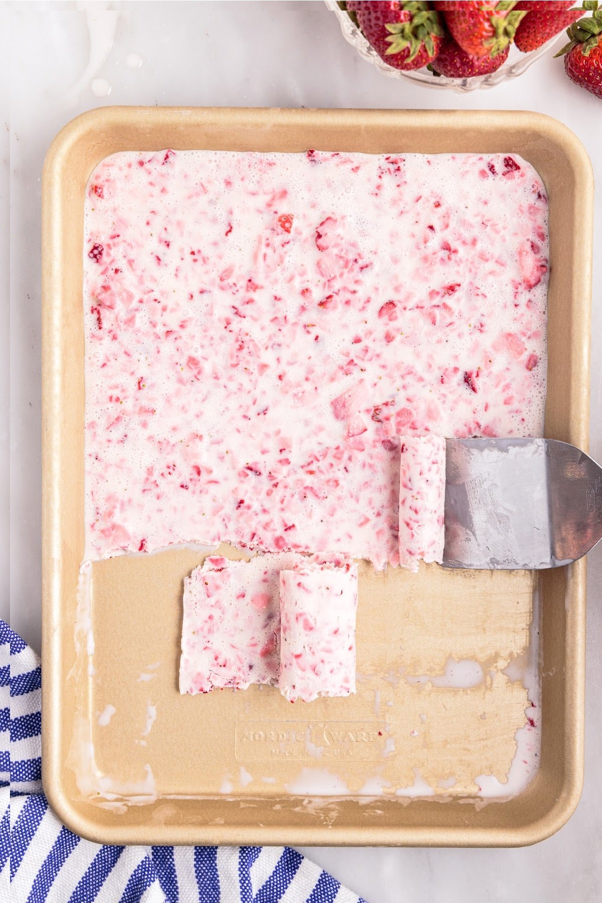 Spatula scraping strawberry ice cream into rolls.