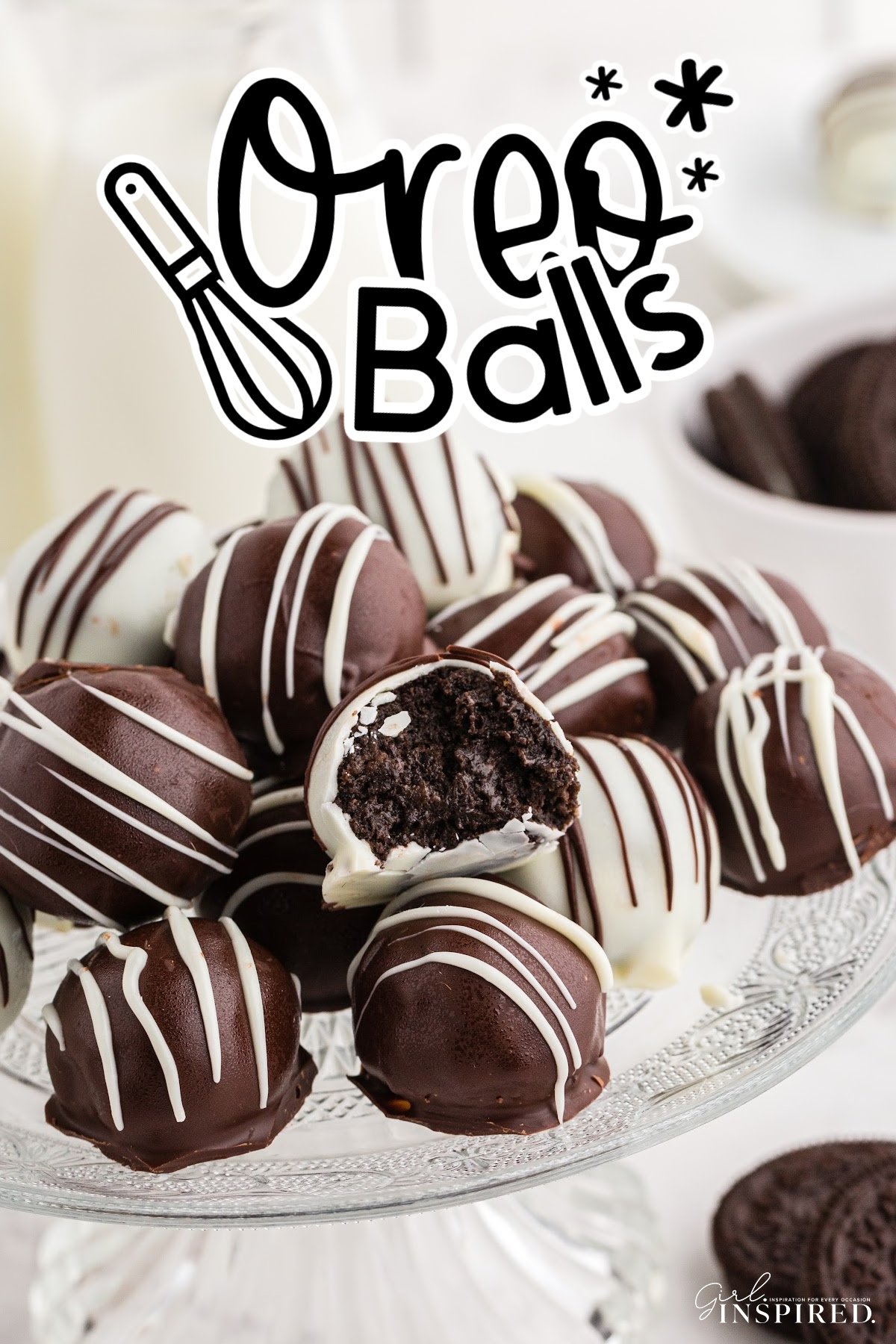 Oreo balls piled on top of each other on a glass cake stand, single Oreo ball broken in half.