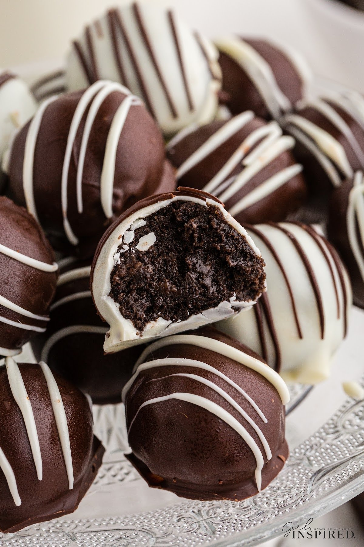 Oreo balls piled on top of each other on a glass cake stand, single Oreo ball broken in half.