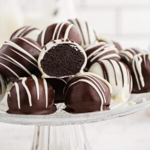 Oreo cookie balls piled on top of each other on a glass cake stand, single Oreo ball cut in half.