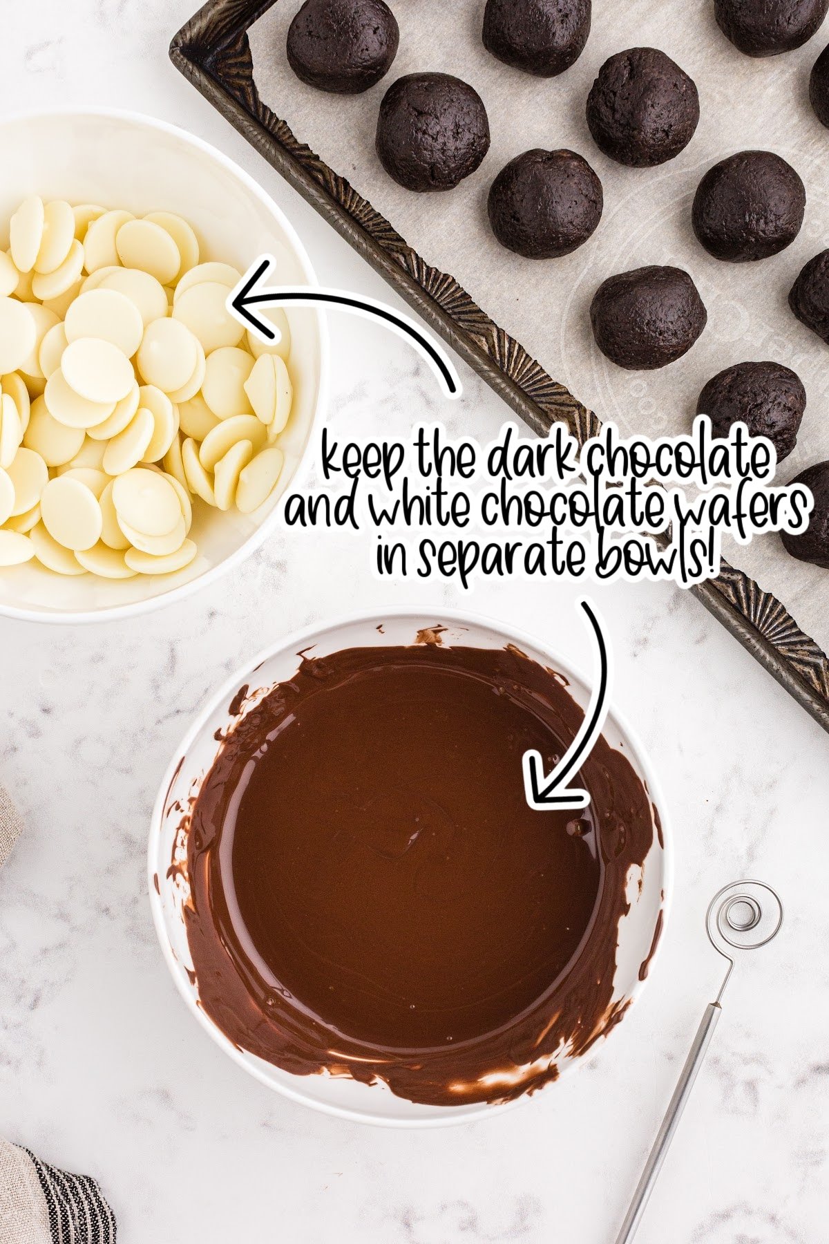 Bowl of melted dark chocolate, bowl of white chocolate melting wafers, tray of frozen Oreo balls, beige linen, on a white marble surface.