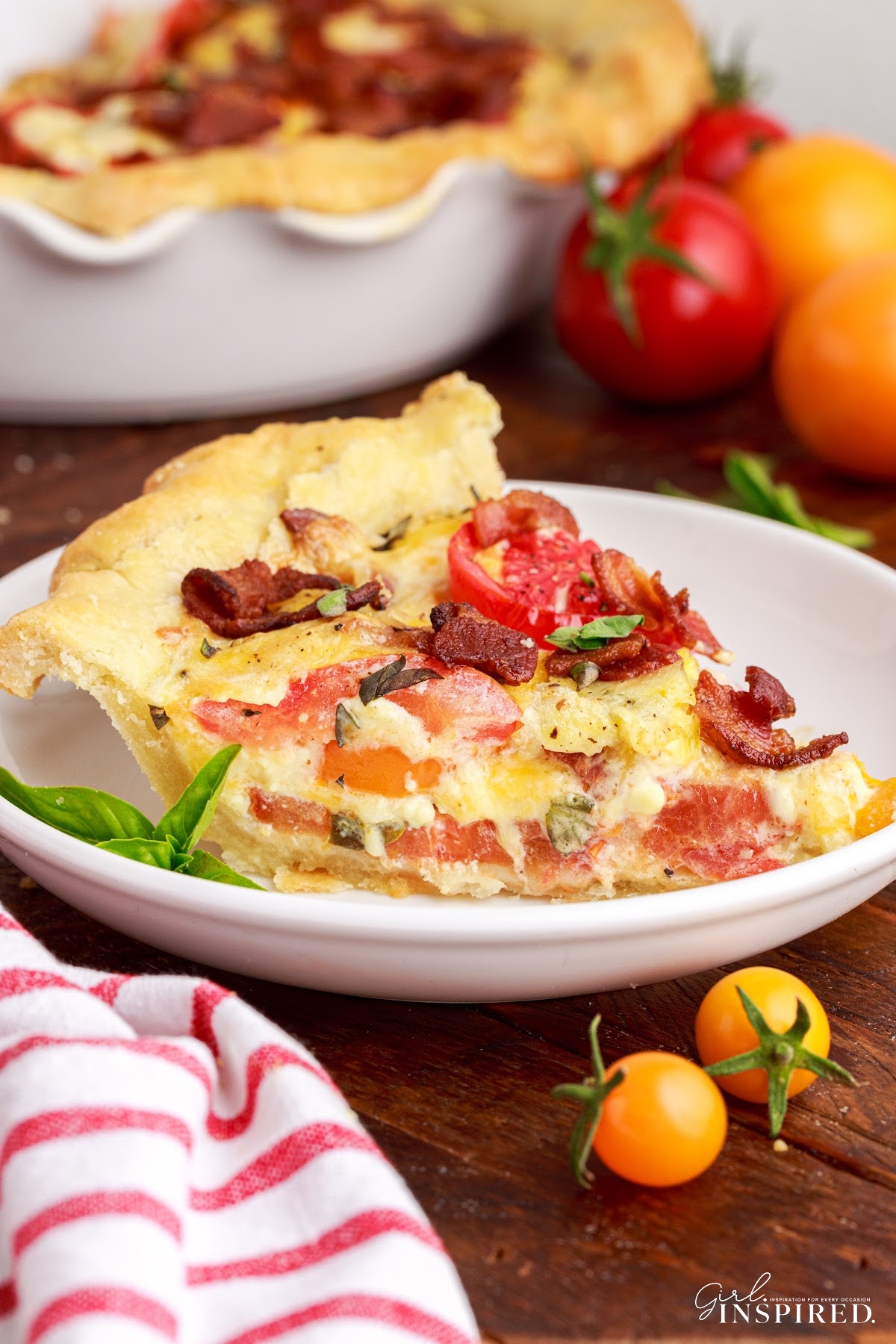 Slice of Southern tomato pie on small plate in front of pie dish and whole tomatoes.