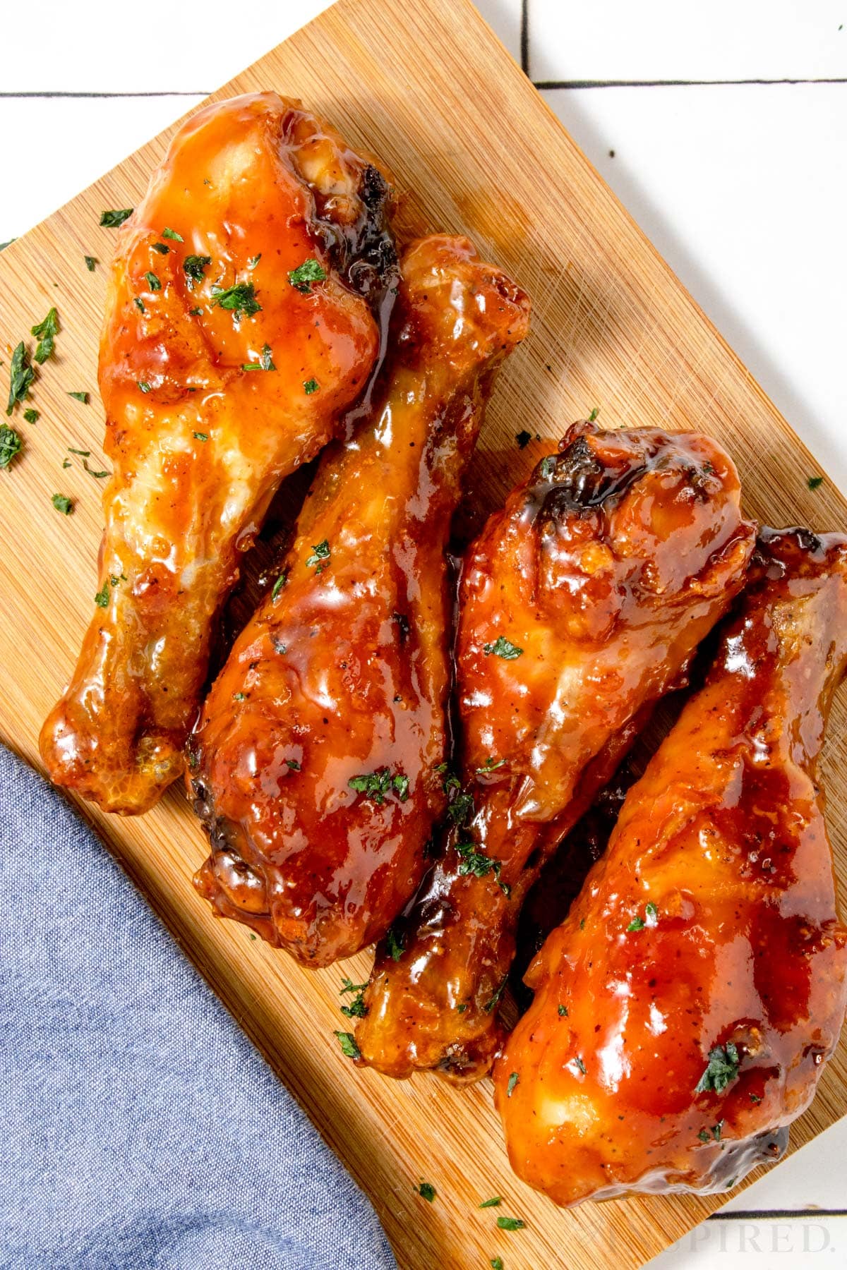 four bbq chicken legs lined up on a wooden cutting board