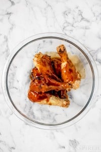bbq chicken legs in a glass mixing bowl covered in sauce