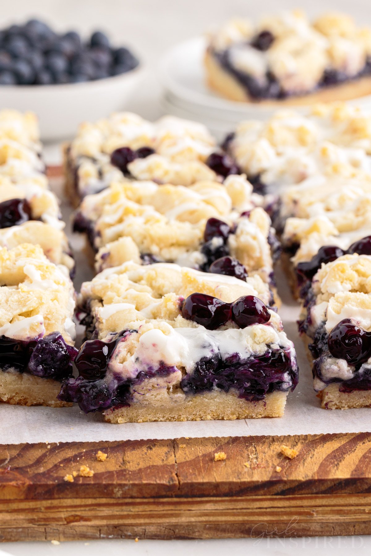 Blueberry pie bars cut into squares on wooden cutting board.