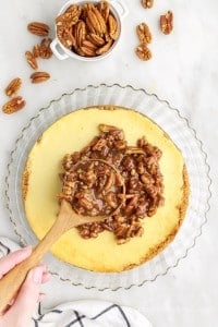pecan caramel sauce spooned on top of the caramel pecan pie cheesecake with a wooden spoon