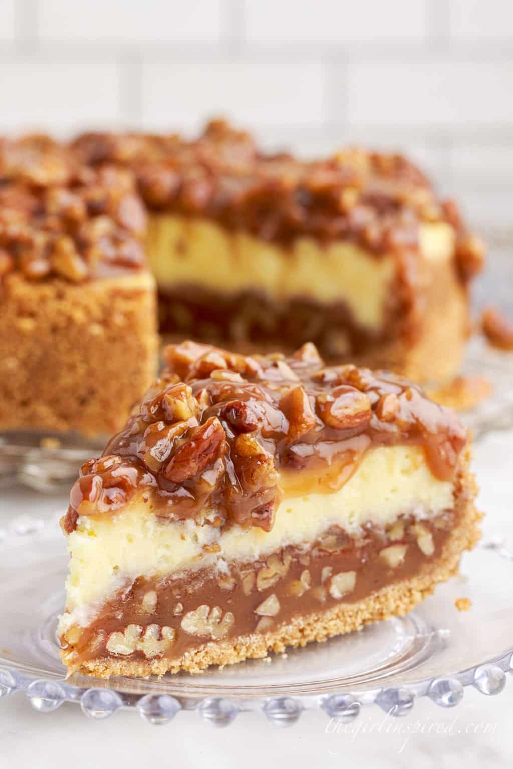 a close up of a slice of caramel pecan pie cheesecake on a glass dish