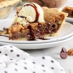 close up of a slice of chocolate chip pie with a scoop of ice cream drizzled with hot fudge