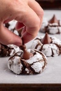 close up of hershey's kiss tip being taken off of a chocolate crackle cookie