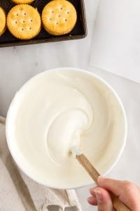 white chocolate chips melted being stirred with a spatula in a white bowl