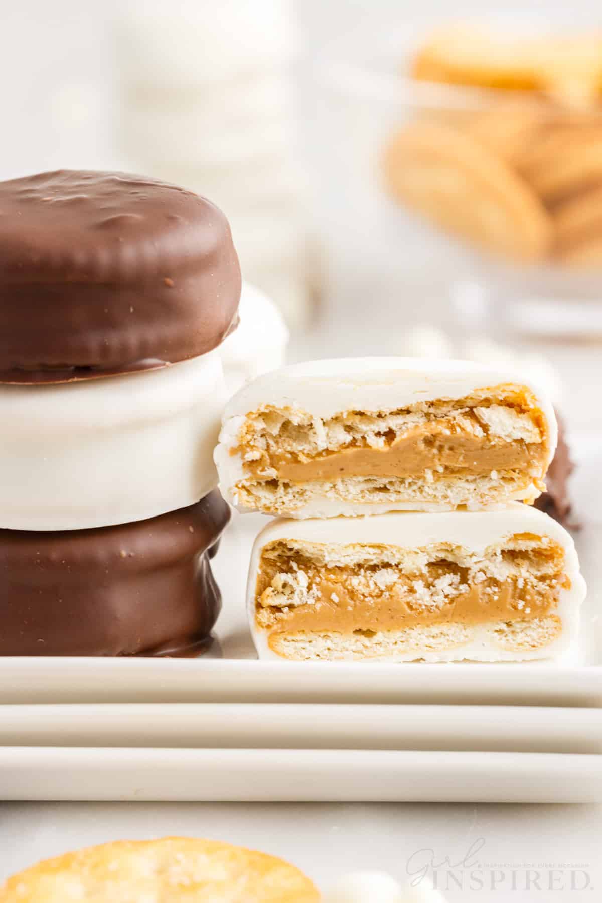 white and milk chocolate dipped peanut butter ritz cookies on stacked white plates one cut in half