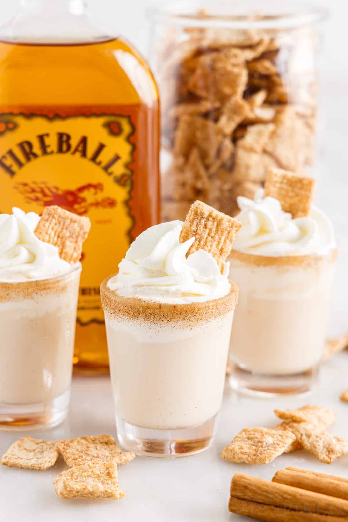 Three cinnamon toast crunch shots with jar of Cinnamon toast crunch cereal and Fireball whiskey.