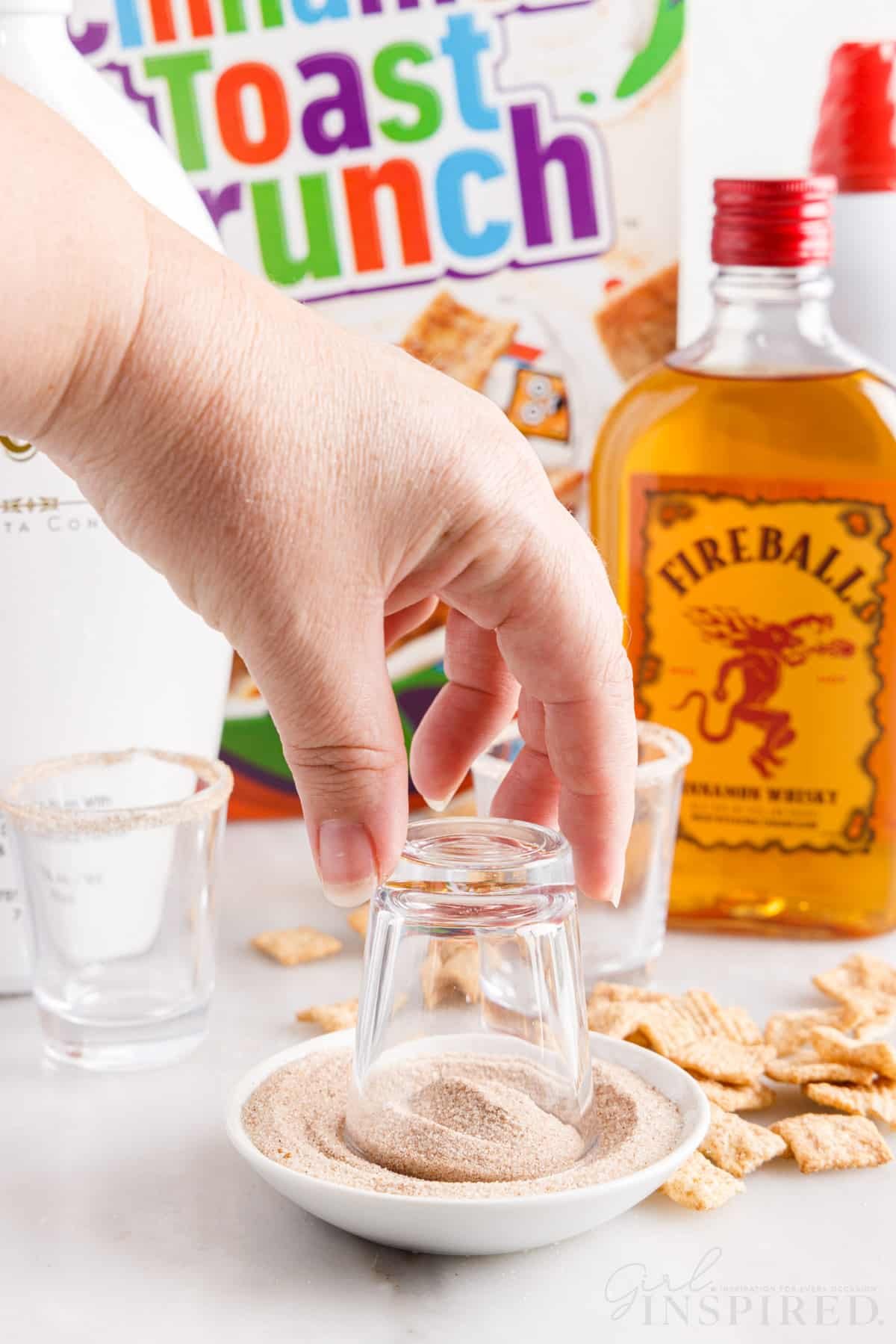 Rim of shot glass dipped in cinnamon sugar with fireball whiskey and cinnamon toast crunch in the background.