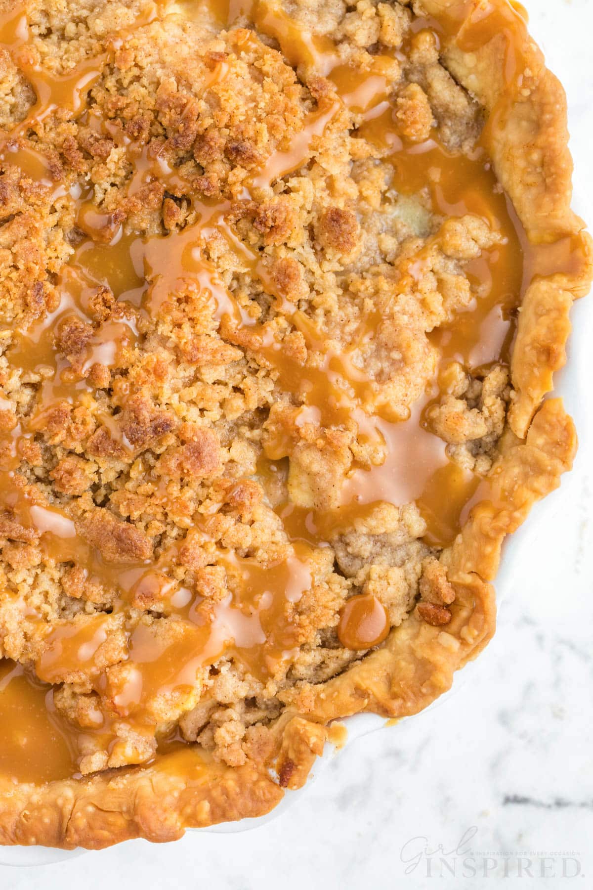 Baked Dutch Caramel Apple Pie with caramel sauce drizzle, on a white marble countertop.