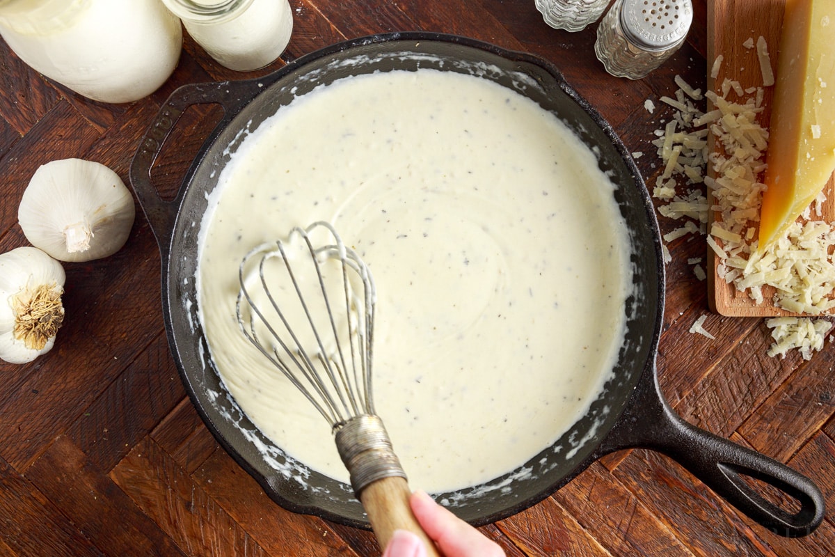 whisk stirring sauce for grilled chicken alfredo in a skillet