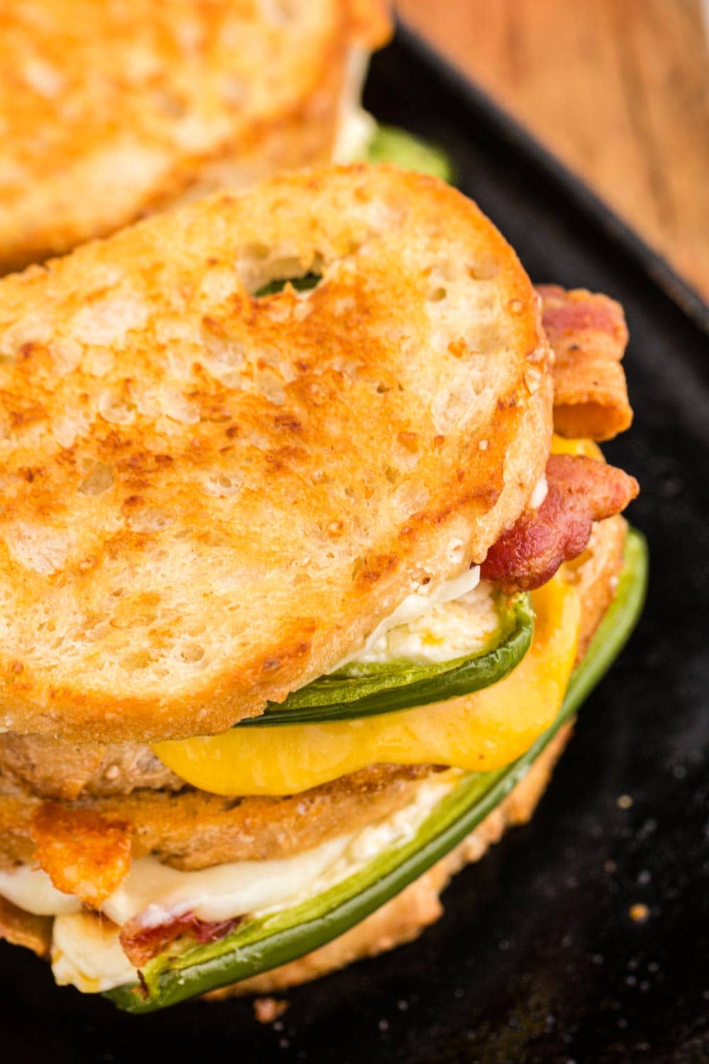 Two Jalapeno popper grilled cheese sandwiches stacked on a skillet.