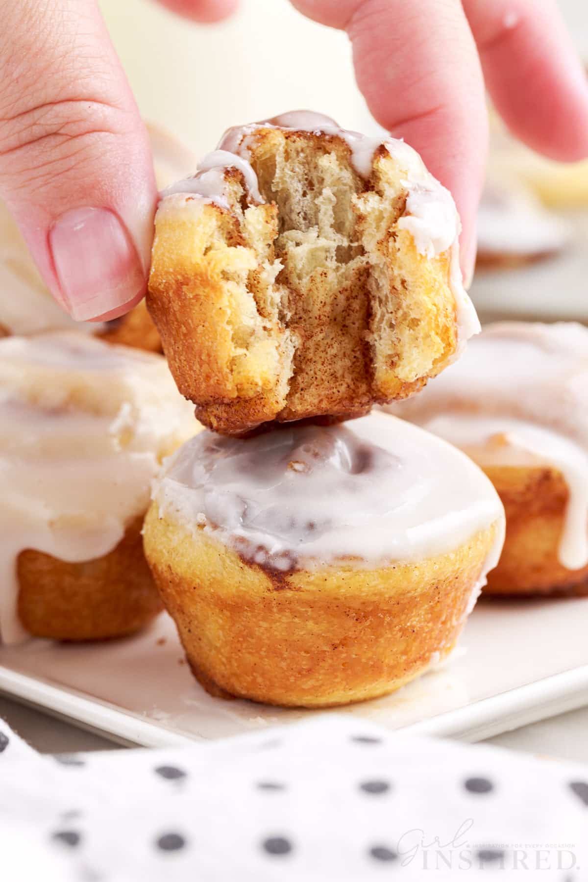 holding a mini cinnamon roll with a bite out of it on top of several others