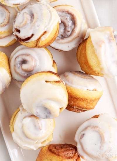 top view of multiple mini cinnamon rolls on an off a white platter