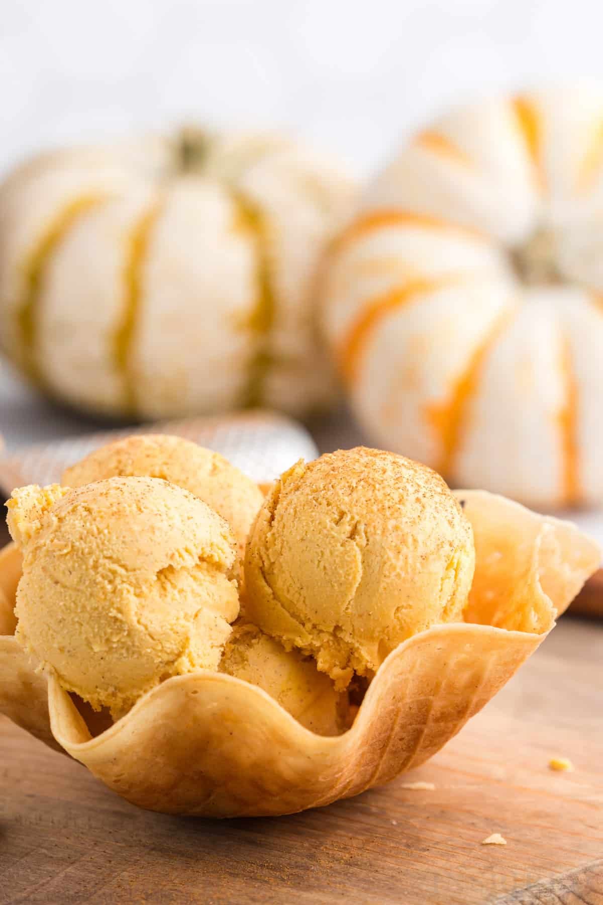 pumpkin ice cream in waffle cone bowl with pumpkins in background.