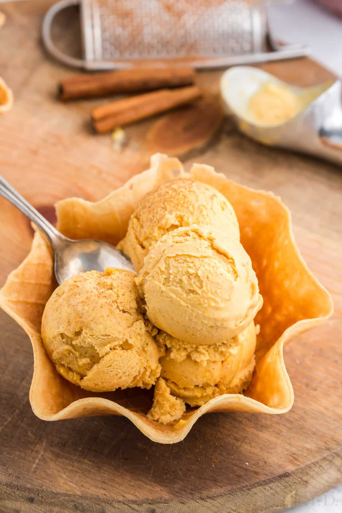 three scoops of pumpkin ice cream piled in a waffle cone bowl with spoon.