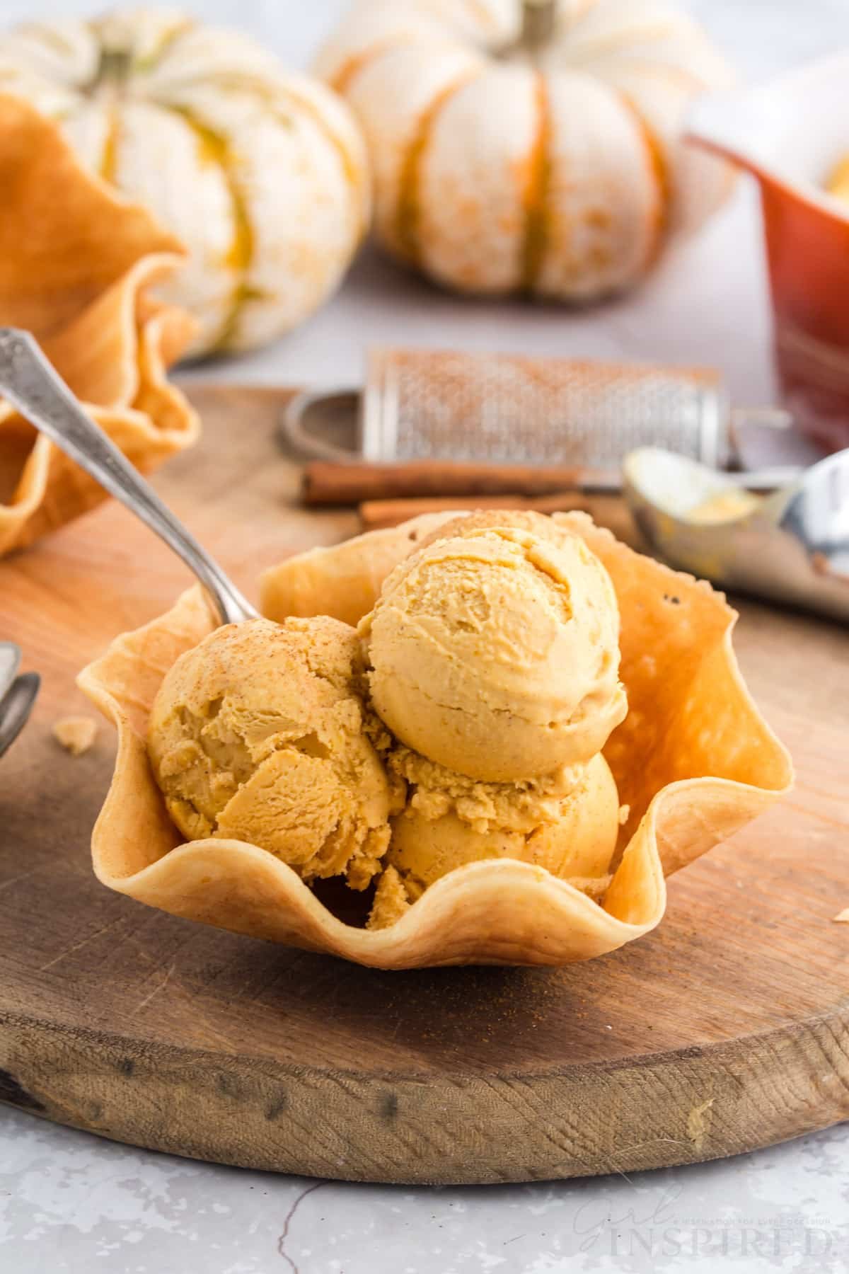 three scoops of pumpkin ice cream piled in a waffle cone bowl with spoon.