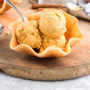 three scoops of pumpkin ice cream piled in a waffle cone bowl with spoon.