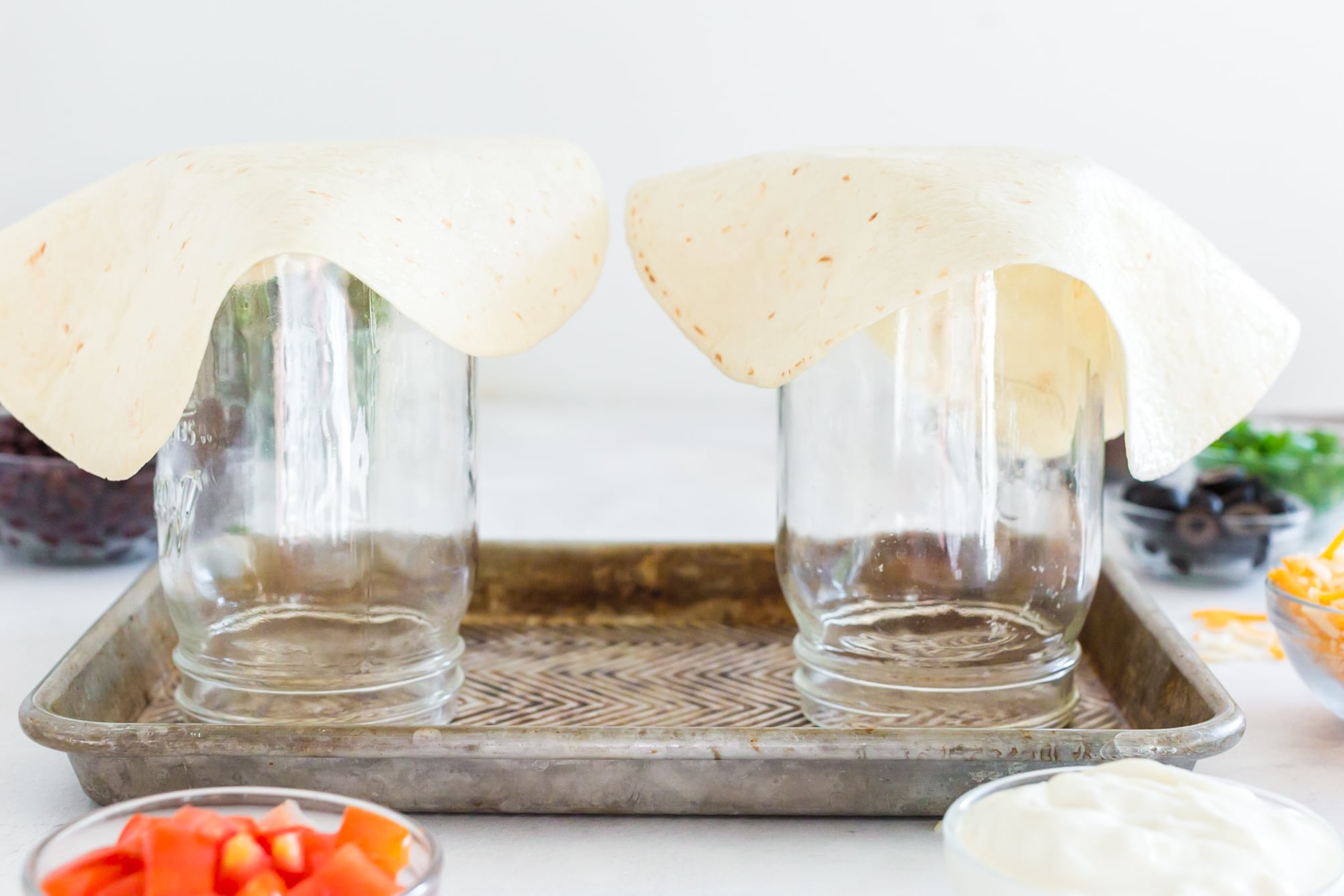 flour tortillas set on top of upside down mason jars on sheet pan.